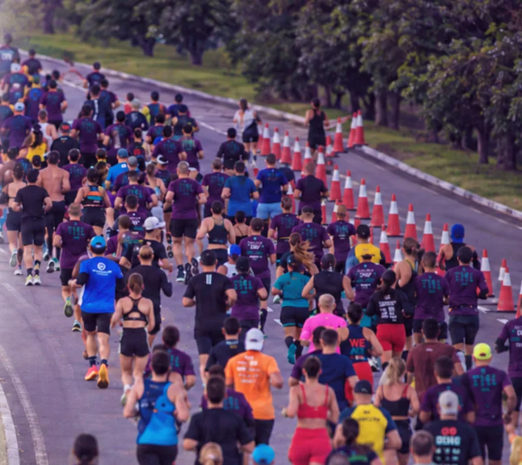 Pelotão da Meia Maratona de Florianópolis 2026 fazendo a curva na avenida, entre cones e árvores