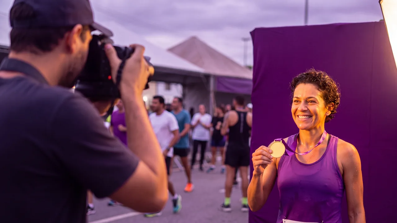 Atleta com a medalha sendo fotografada diante de um painel na chegada