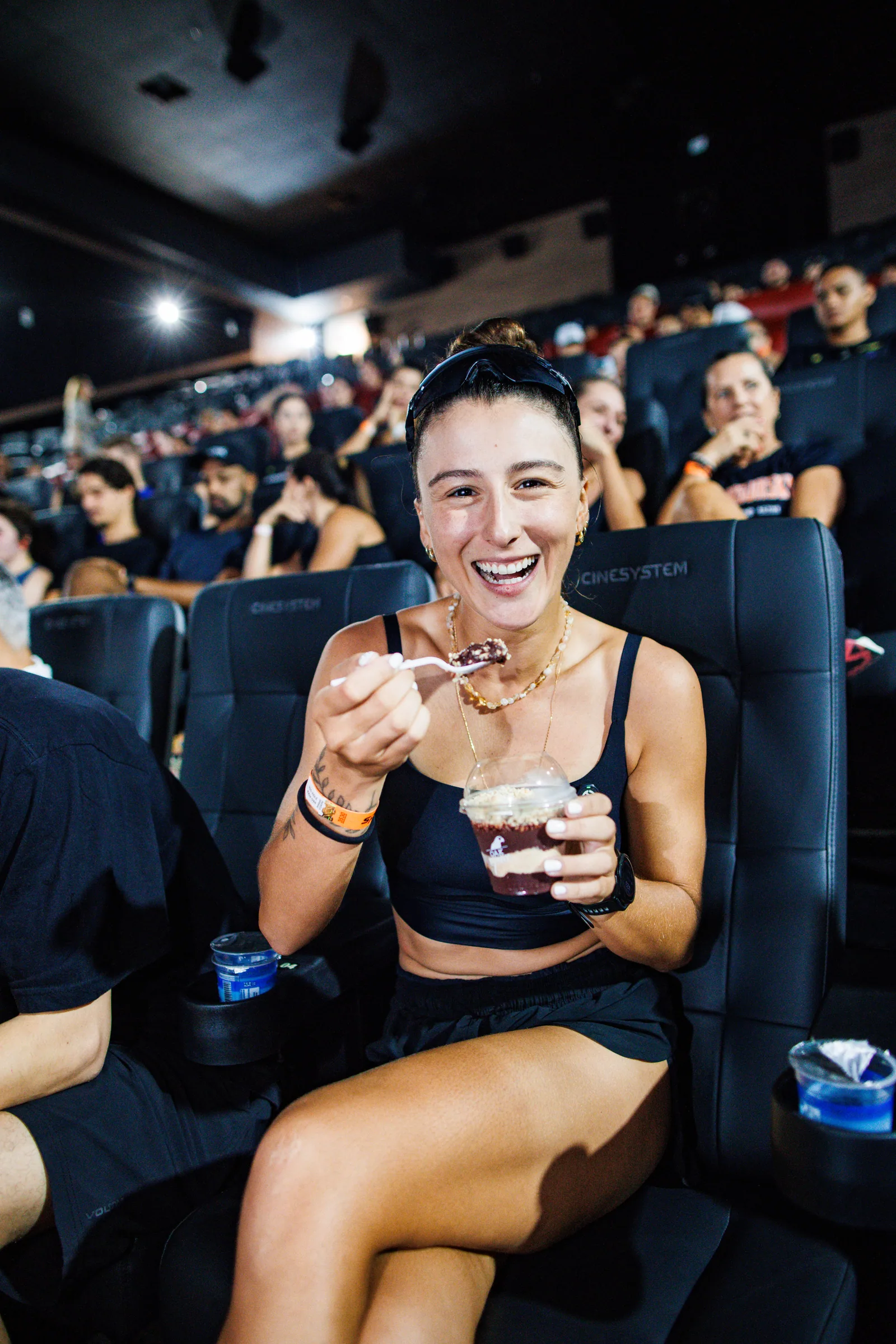 Corredora ri com o copo de açaí Oakberry na poltrona do cinema, depois do treinão