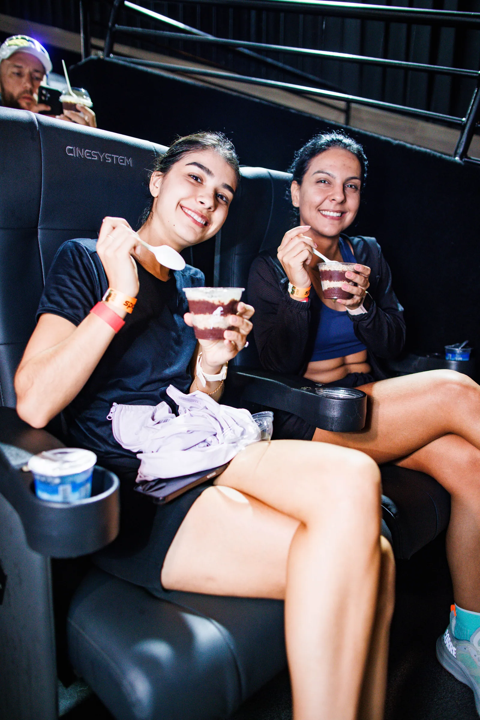 Duas amigas com copos de açaí Oakberry nas poltronas do cinema