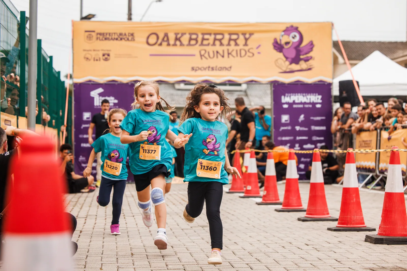 Crianças disparam sob o pórtico da Oakberry Run Kids, entre cones, com o público nos gradis