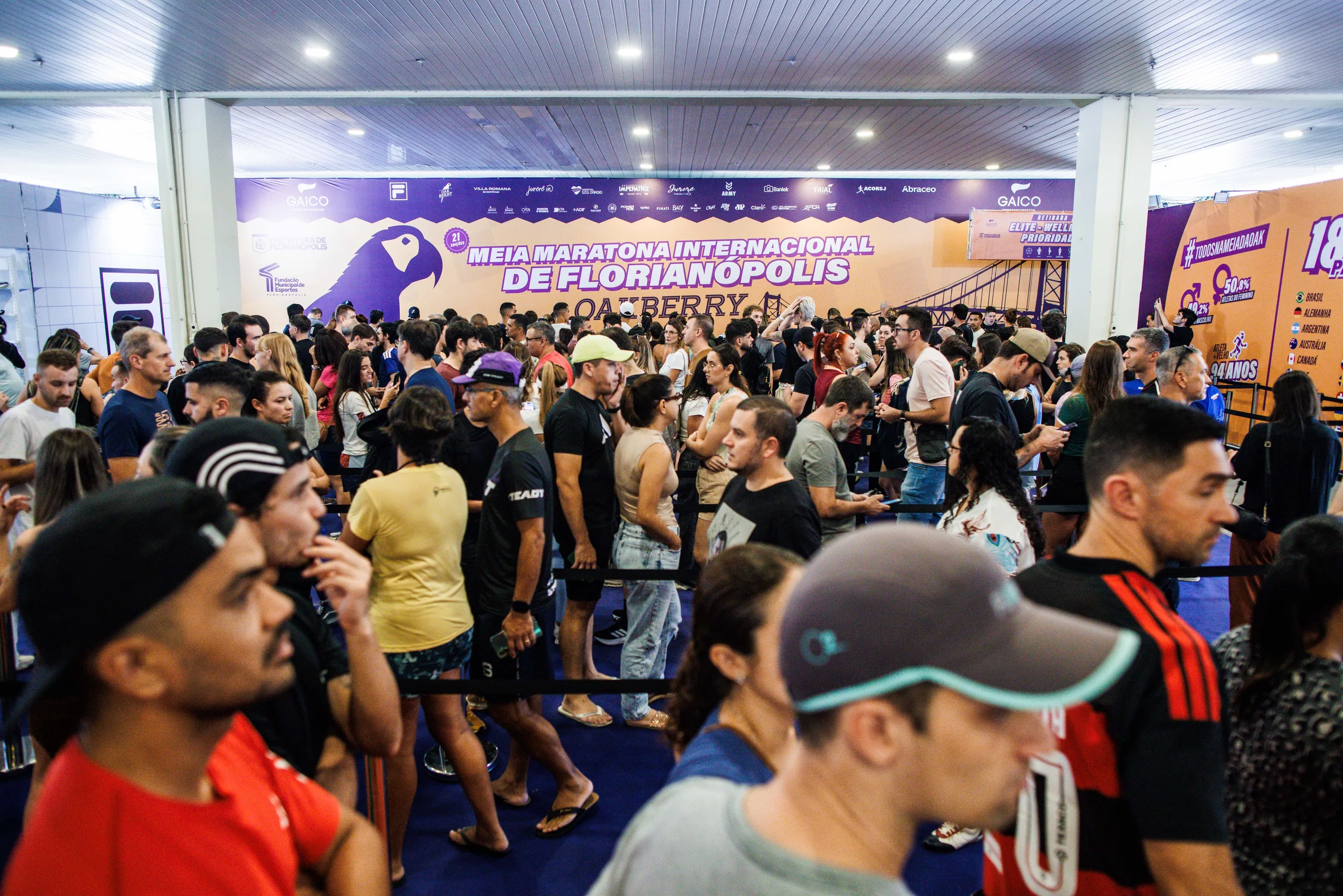Multidão na área de retirada de kits da Oakvillage, sob o painel da Meia Maratona Internacional de Florianópolis Oakberry