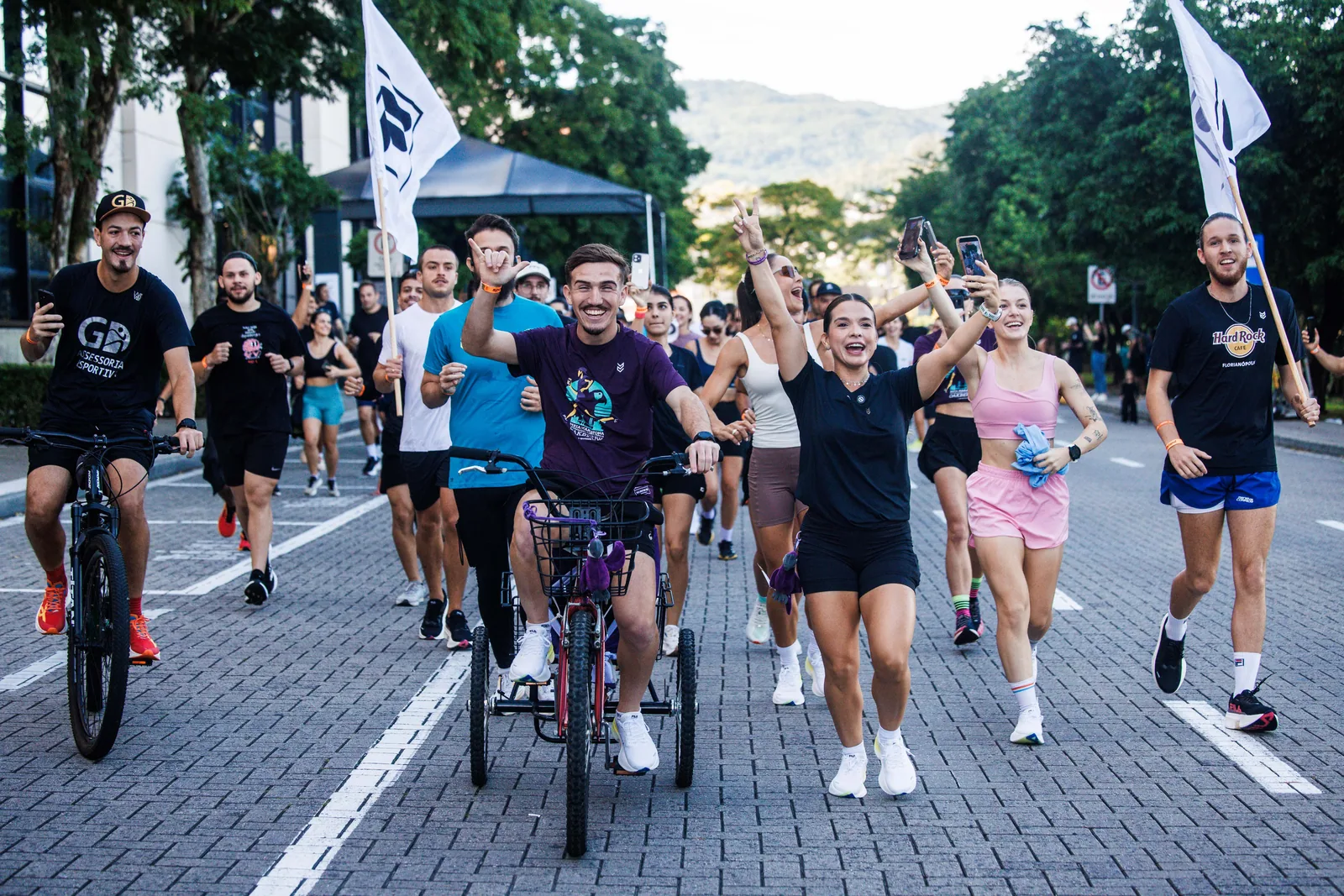 Treinão na rua: corredores com bandeiras FILA, ciclistas e triciclo, morros ao fundo